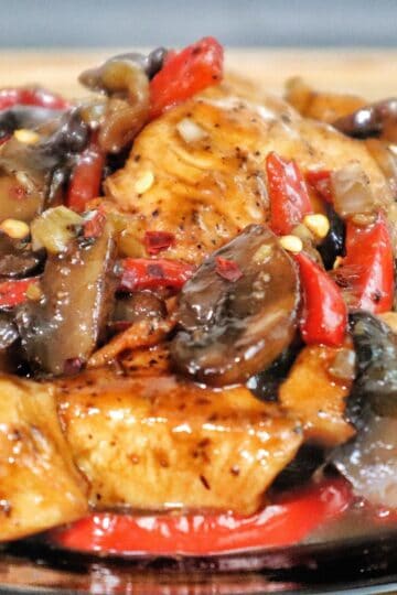 Black Pepper Chicken with Mushrooms served on a black plate, with seared chicken strips, sautéed red and green bell peppers, and mushrooms coated in a black pepper sauce.