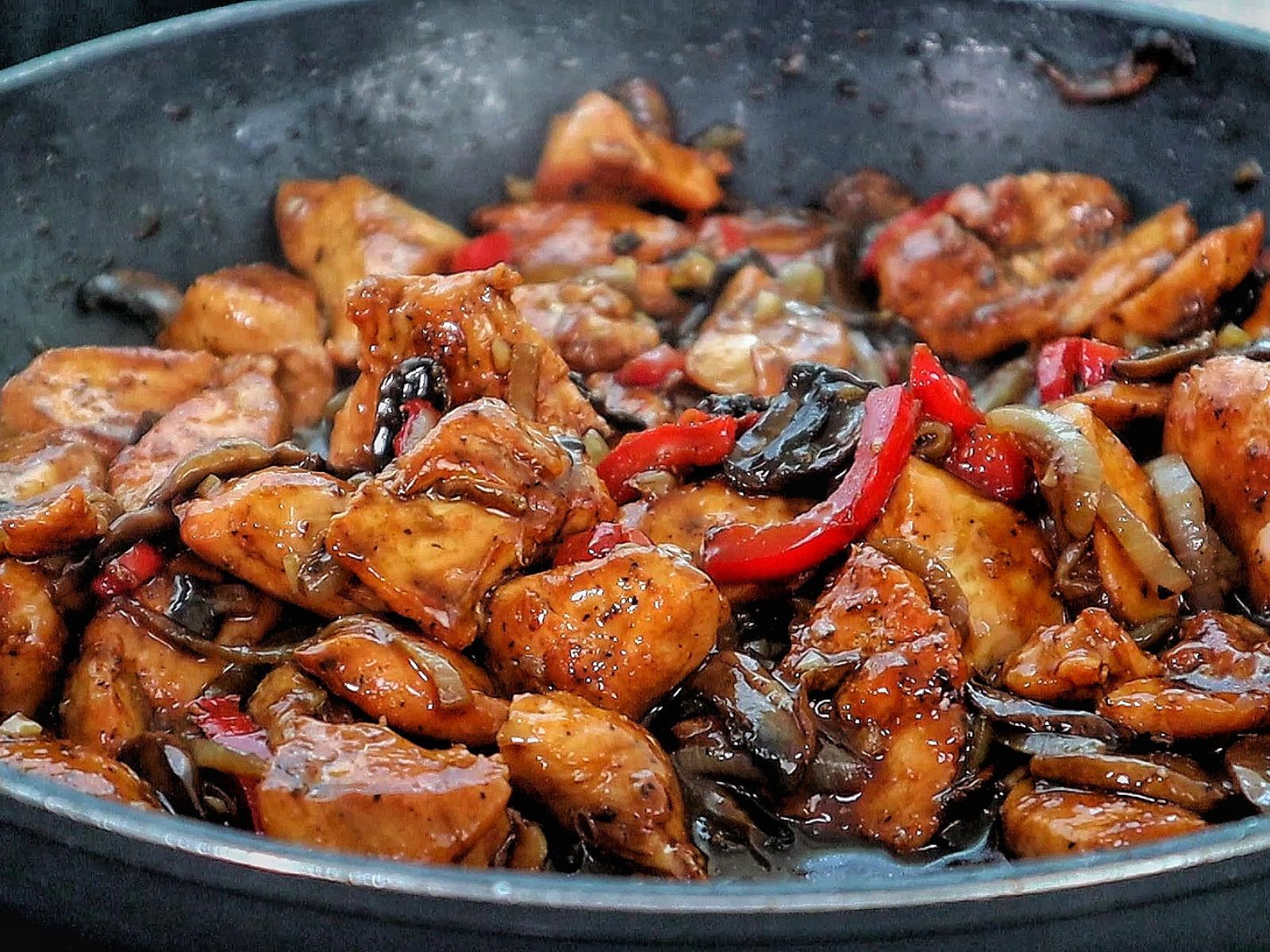 Black Pepper Chicken with Mushrooms served on a black plate, with seared chicken strips, sautéed red and green bell peppers, and mushrooms coated in a black pepper sauce.