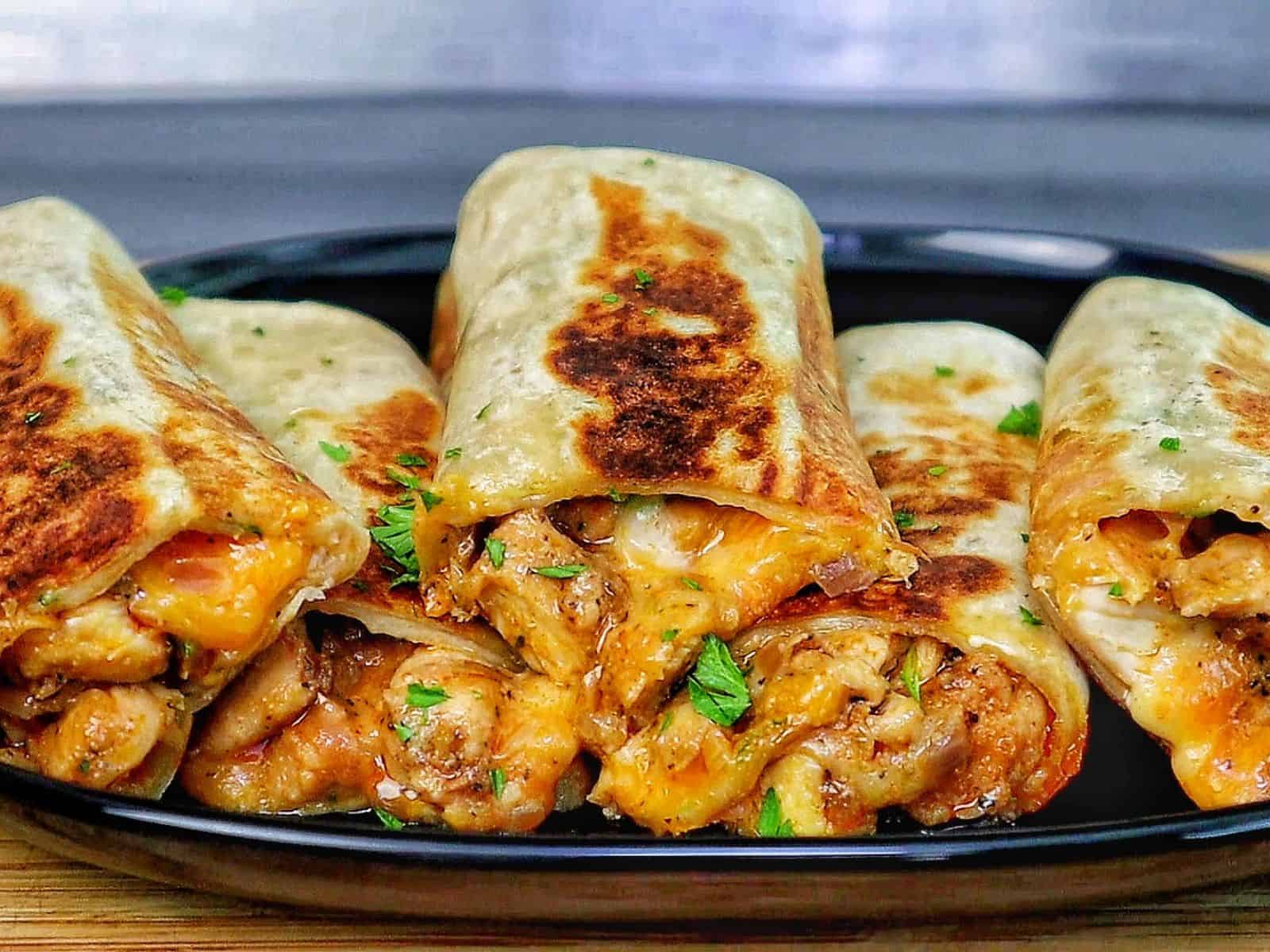 Golden-brown cheesy garlic chicken wraps, stuffed with melted cheese and tender chicken served on a black plate.