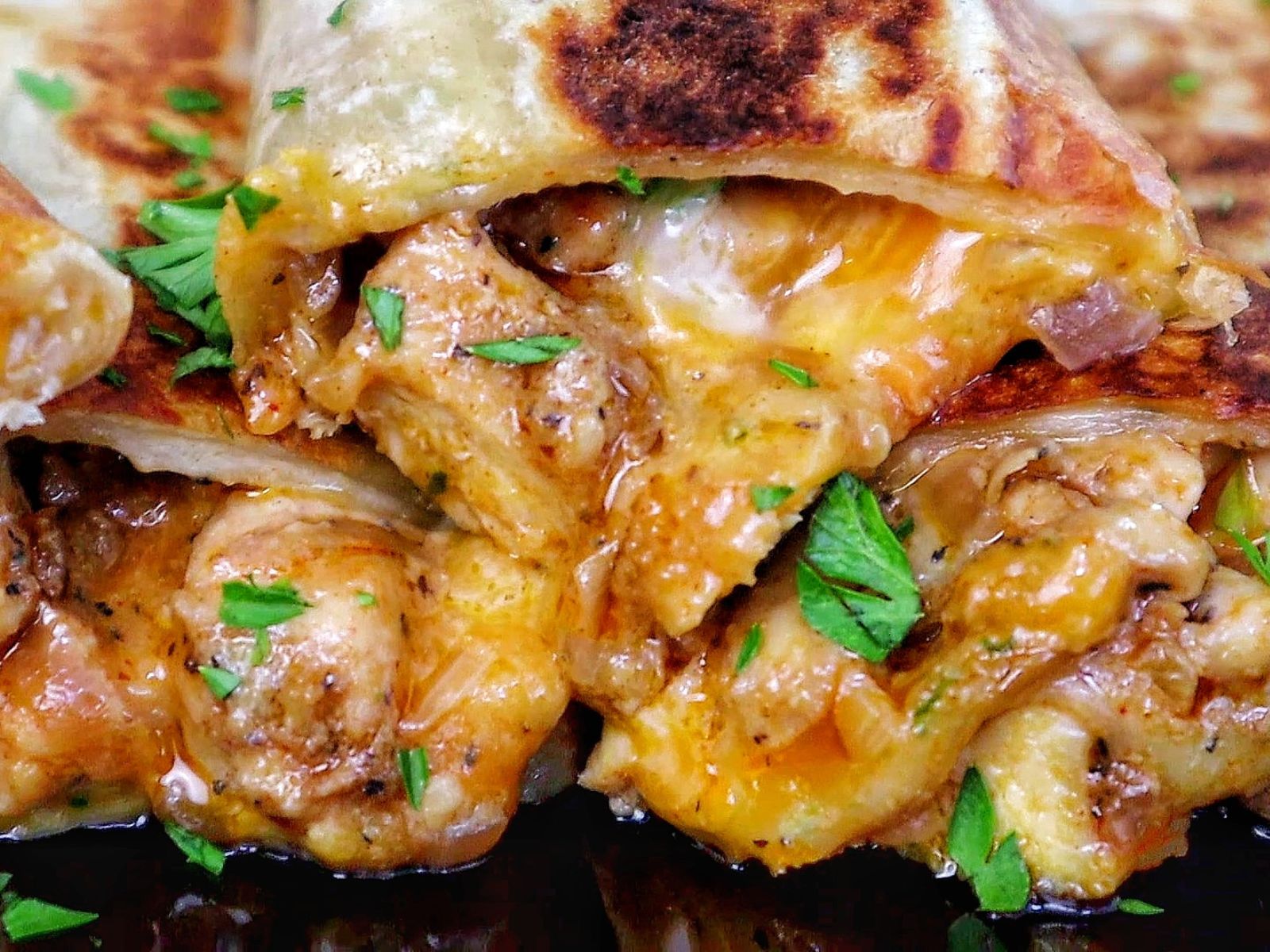 Golden-brown grilled cheesy garlic chicken wraps, stuffed with melted cheese and tender chicken served on a black plate.