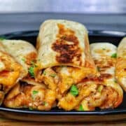 Golden-brown cheesy garlic chicken wraps, stuffed with melted cheese and tender chicken served on a black plate.