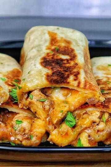 Golden-brown cheesy garlic chicken wraps, stuffed with melted cheese and tender chicken served on a black plate.