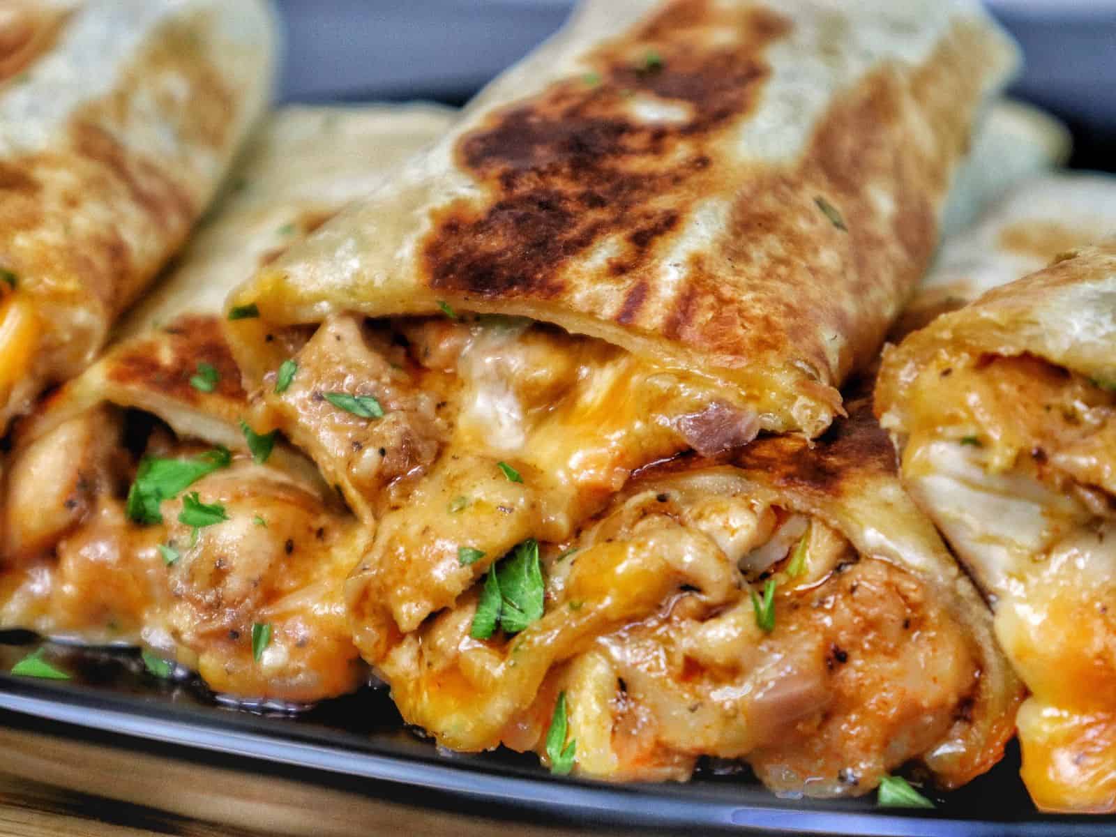 Golden-brown cheesy garlic chicken wraps, stuffed with melted cheese and tender chicken served on a black plate.