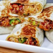 A stack of grilled chili cheese burritos, stuffed with seasoned ground beef, melted cheese, rice, beans, and sliced jalapeños.