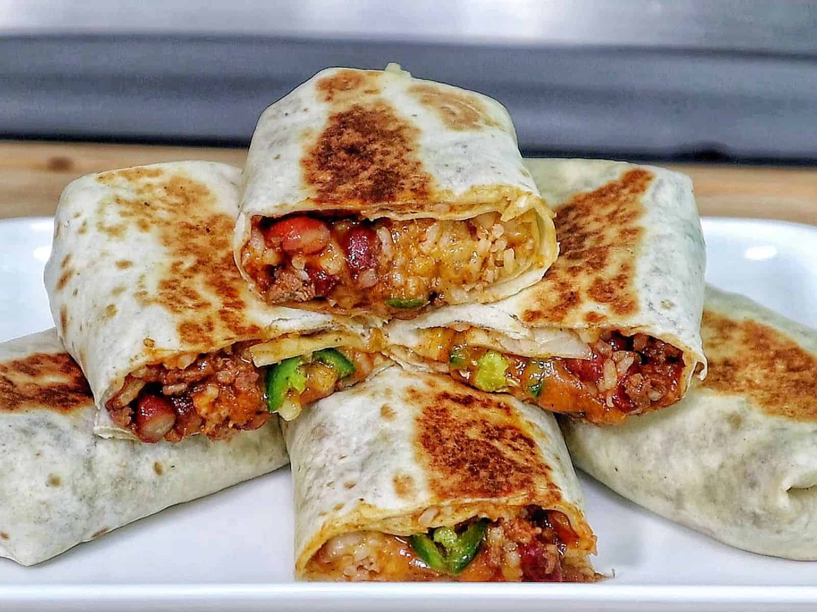 A stack of grilled chili cheese burritos, stuffed with seasoned ground beef, melted cheese, rice, beans, and sliced jalapeños.