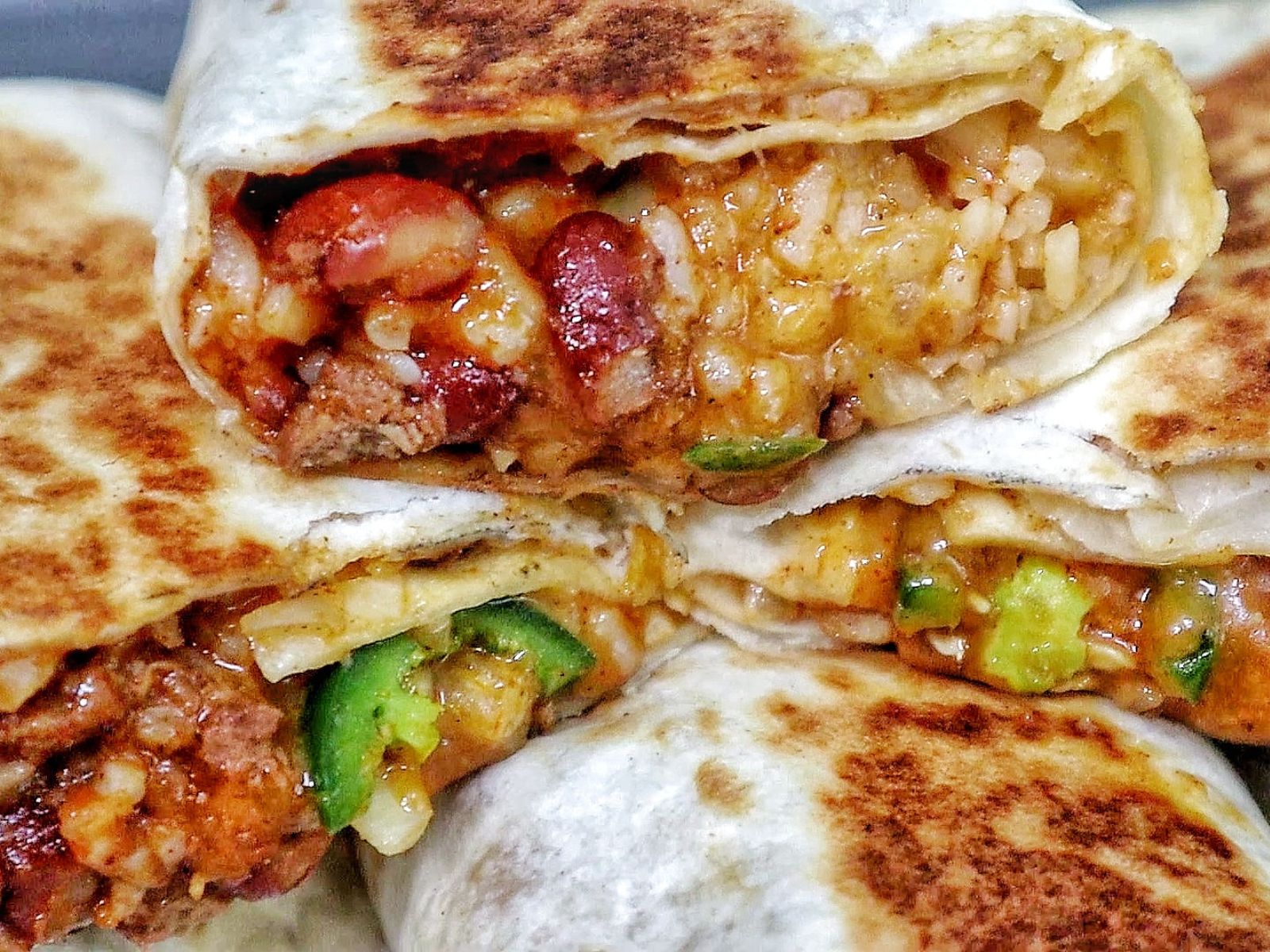 A stack of grilled chili cheese burritos, stuffed with seasoned ground beef, melted cheese, rice, beans, and sliced jalapeños.