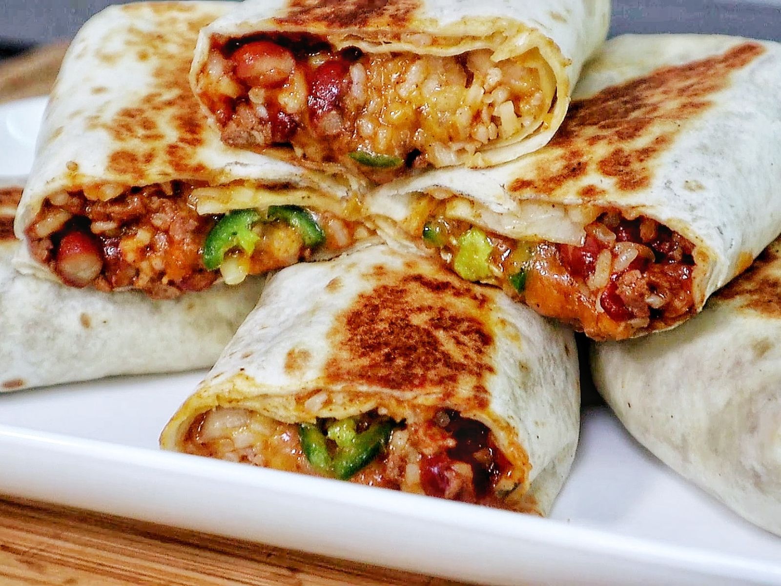 A stack of grilled chili cheese burritos, stuffed with seasoned ground beef, melted cheese, rice, beans, and sliced jalapeños.