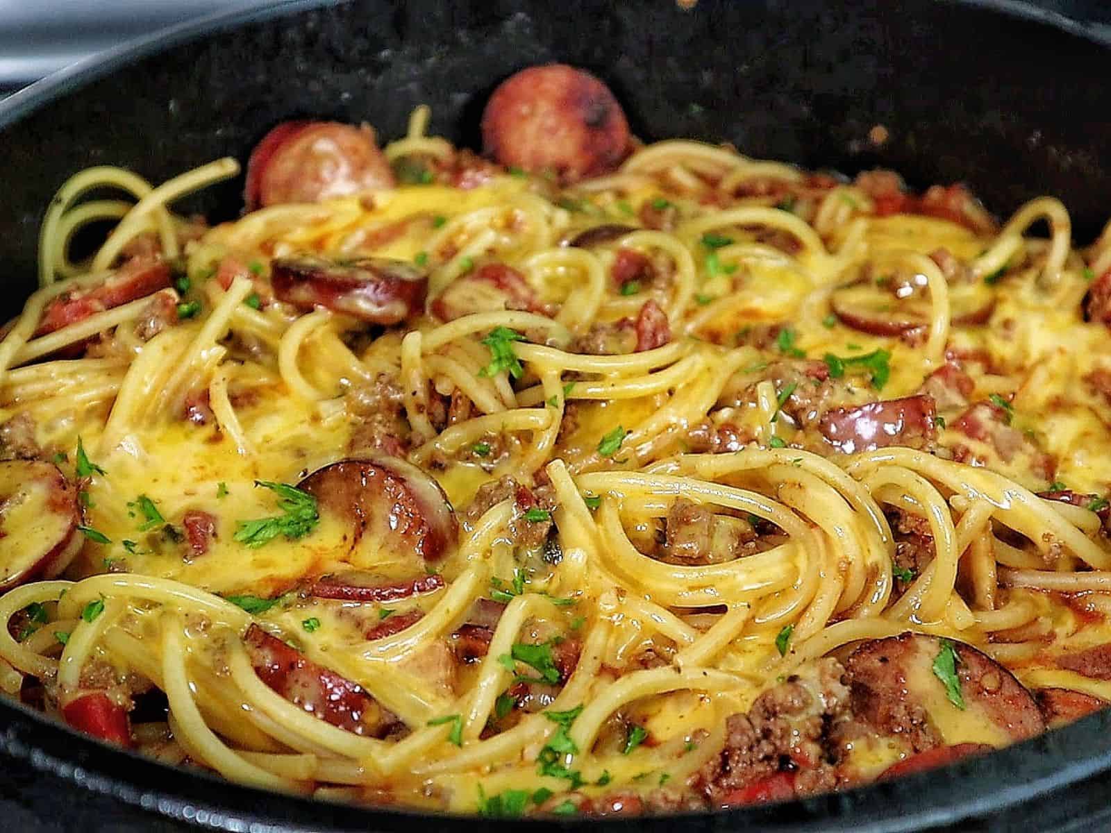 Cheesy cowboy spaghetti made with spaghetti noodles, slices of polish sausage, ground beef, diced tomatoes, and melted cheddar cheese, garnished with fresh parsley.