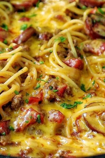 Cheesy cowboy spaghetti made with spaghetti noodles, slices of polish sausage, ground beef, diced tomatoes, and melted cheddar cheese, garnished with fresh parsley.