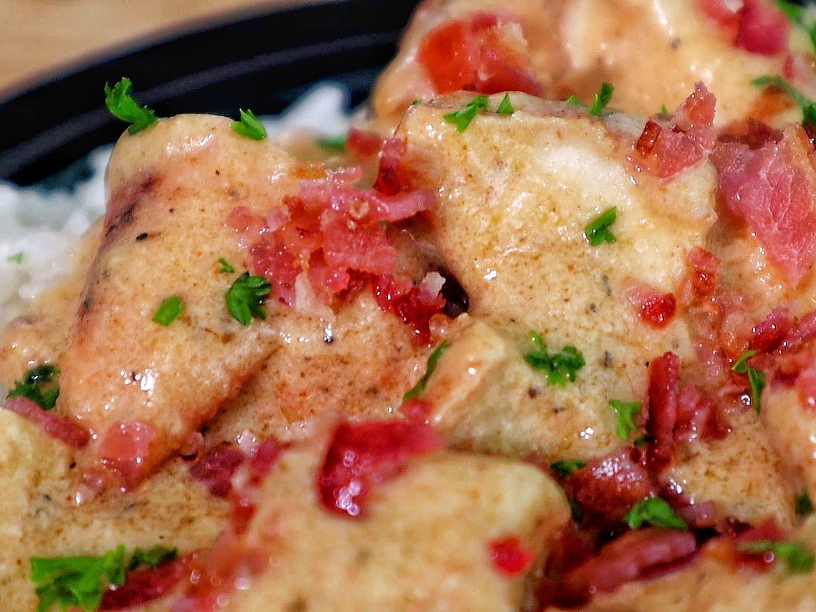 Creamy smothered chicken served over a bed of fluffy white rice, topped with crumbled bacon and chopped parsley for garnish.