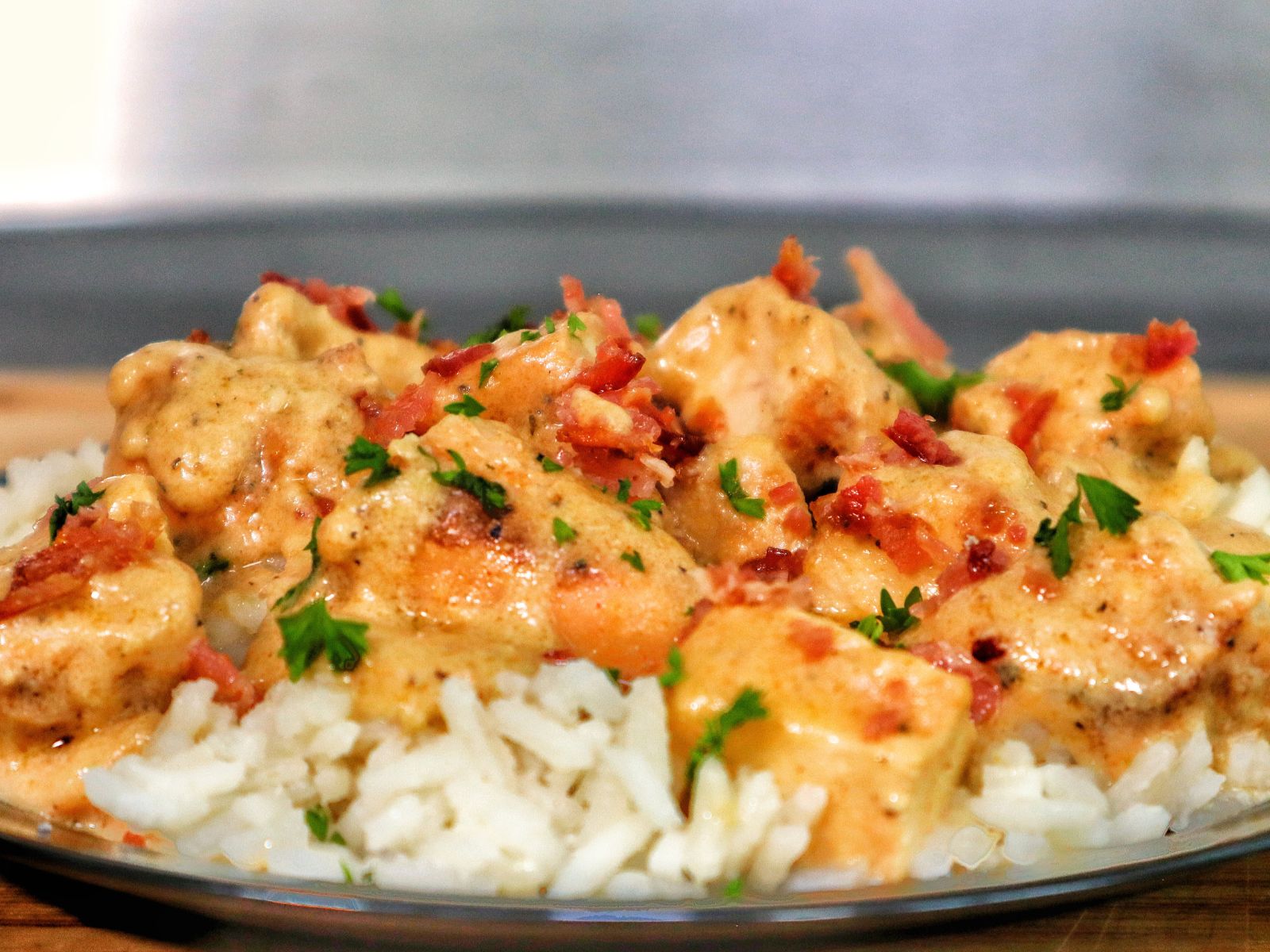 Creamy smothered chicken served over a bed of fluffy white rice, topped with crumbled bacon and chopped parsley for garnish.