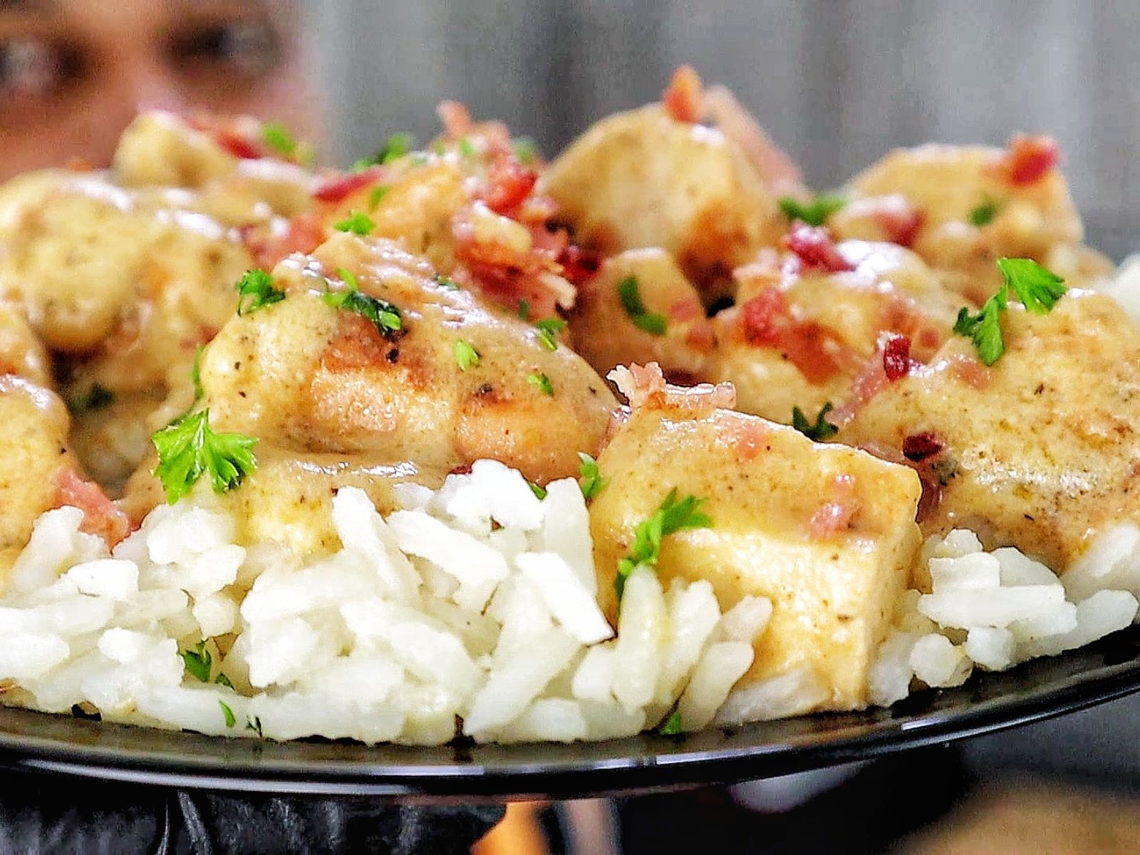 Creamy smothered chicken served over a bed of fluffy white rice, topped with crumbled bacon and chopped parsley for garnish.