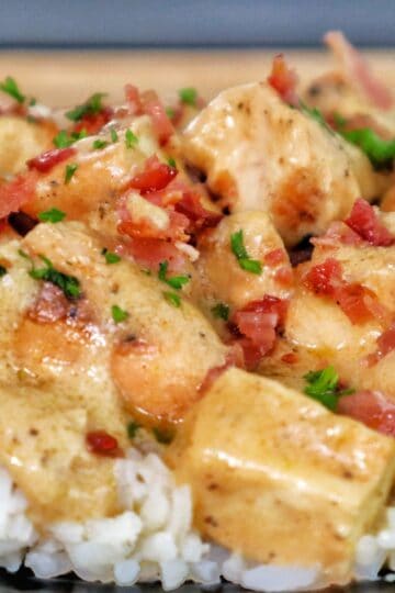 Creamy smothered chicken served over a bed of fluffy white rice, topped with crumbled bacon and chopped parsley for garnish.