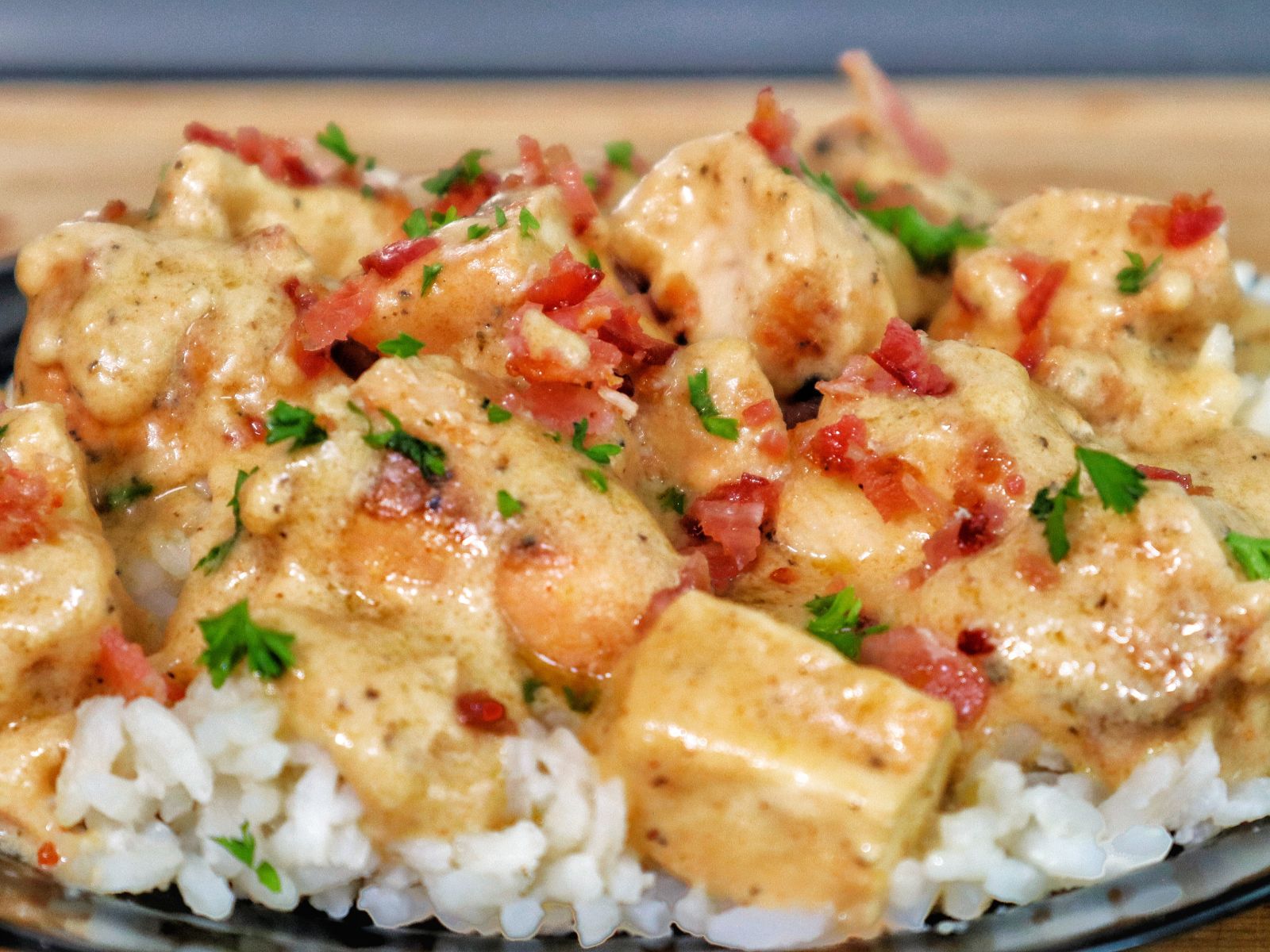 Creamy smothered chicken served over a bed of fluffy white rice, topped with crumbled bacon and chopped parsley for garnish.