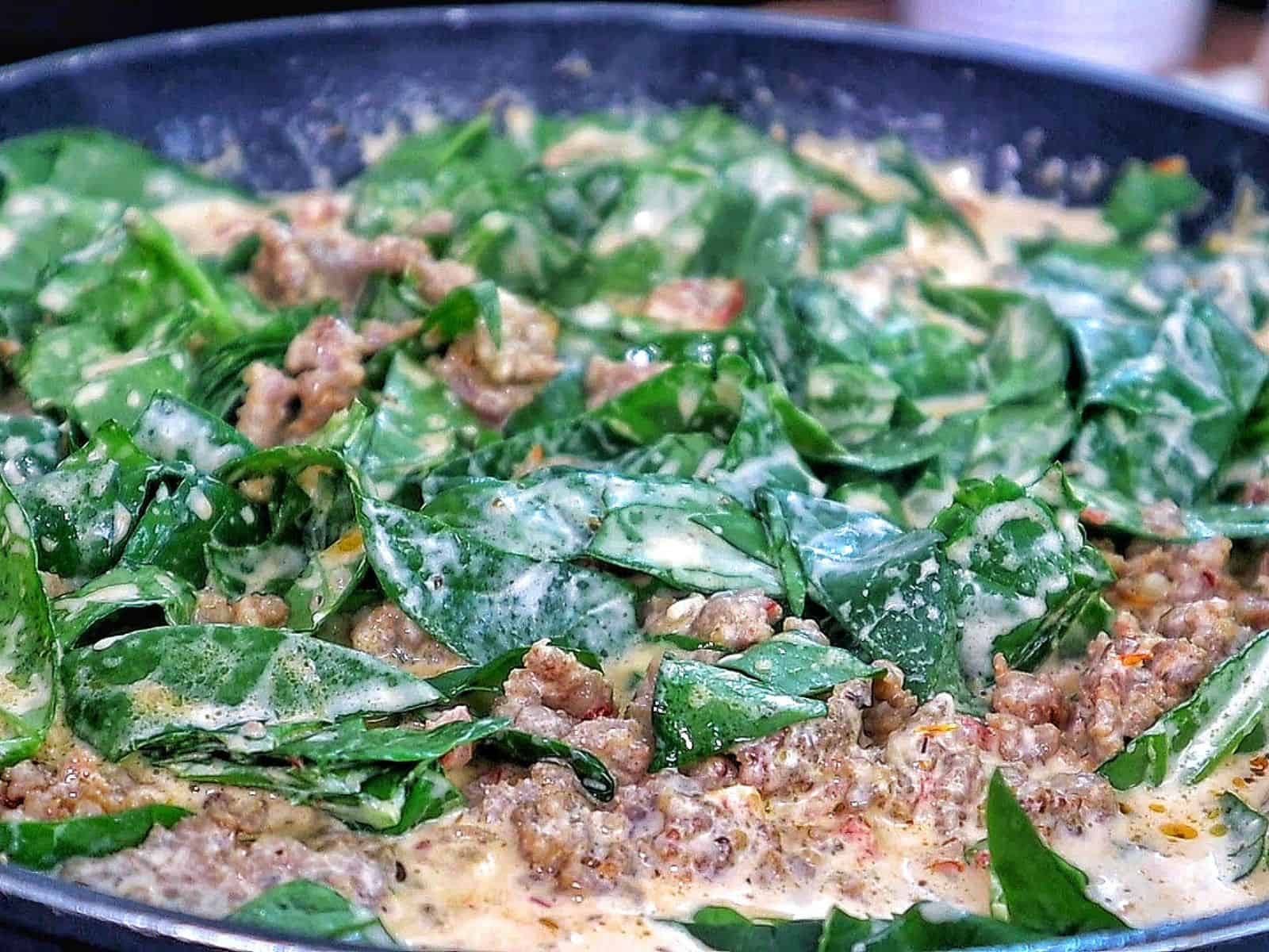 A skillet filled with creamy Tuscan sausage pasta made with penne, Italian sausage, sun-dried tomatoes, and fresh spinach, coated in a rich cream sauce and garnished with fresh basil.