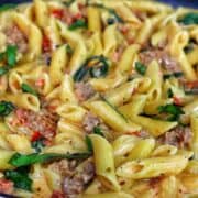 A skillet filled with creamy Tuscan sausage pasta made with penne, Italian sausage, sun-dried tomatoes, and fresh spinach, coated in a rich cream sauce and garnished with fresh basil.