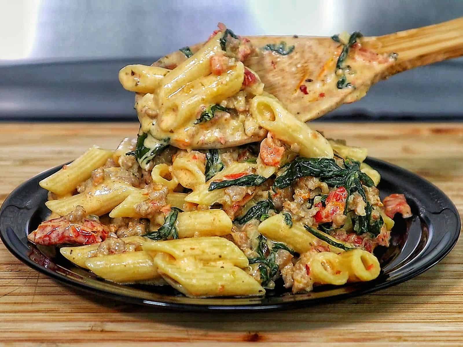 A skillet filled with creamy Tuscan sausage pasta made with penne, Italian sausage, sun-dried tomatoes, and fresh spinach, coated in a rich cream sauce and garnished with fresh basil.