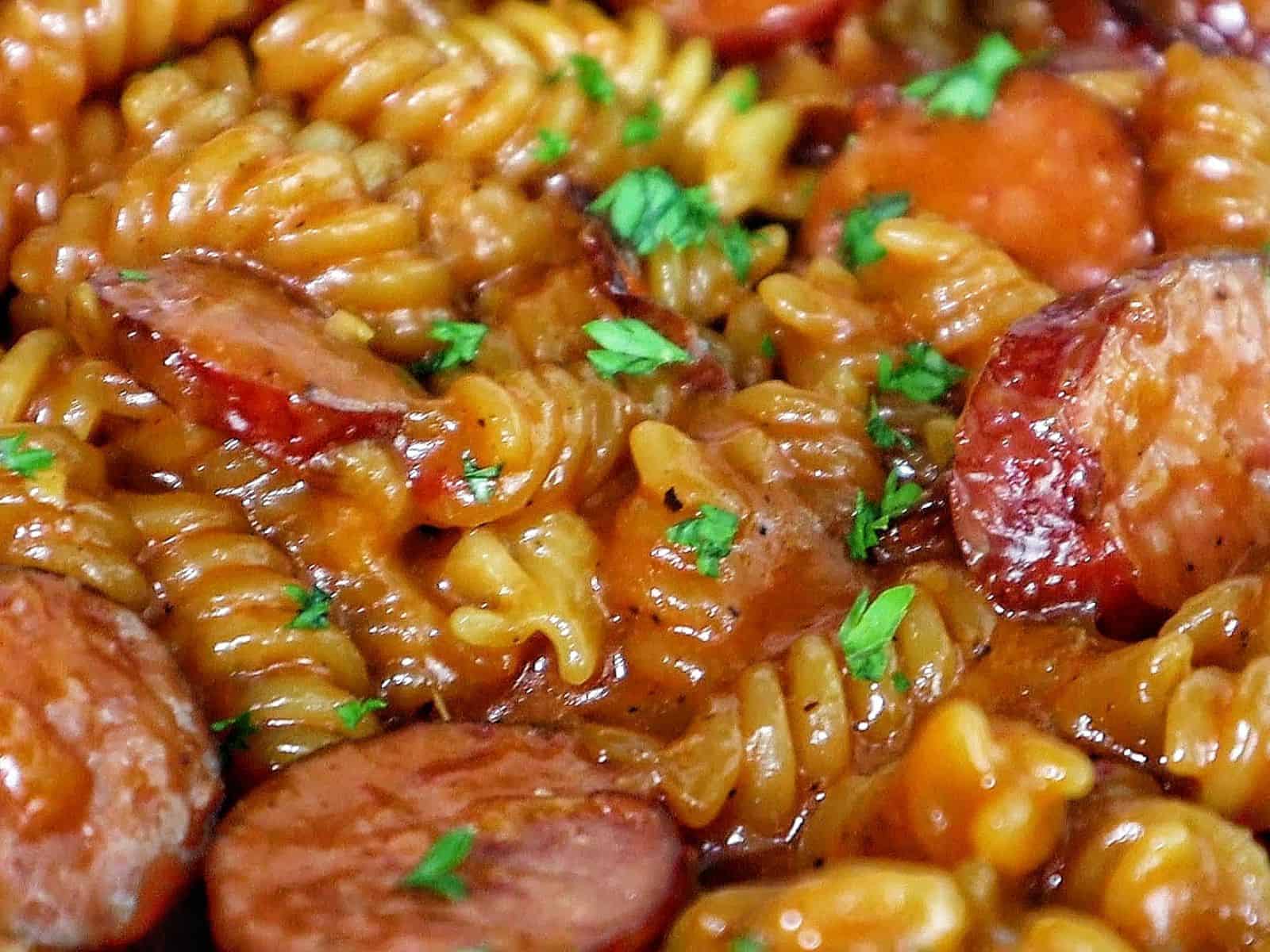 rotini pasta coated in a rich honey BBQ sauce with sliced sausage and garnished with fresh parsley