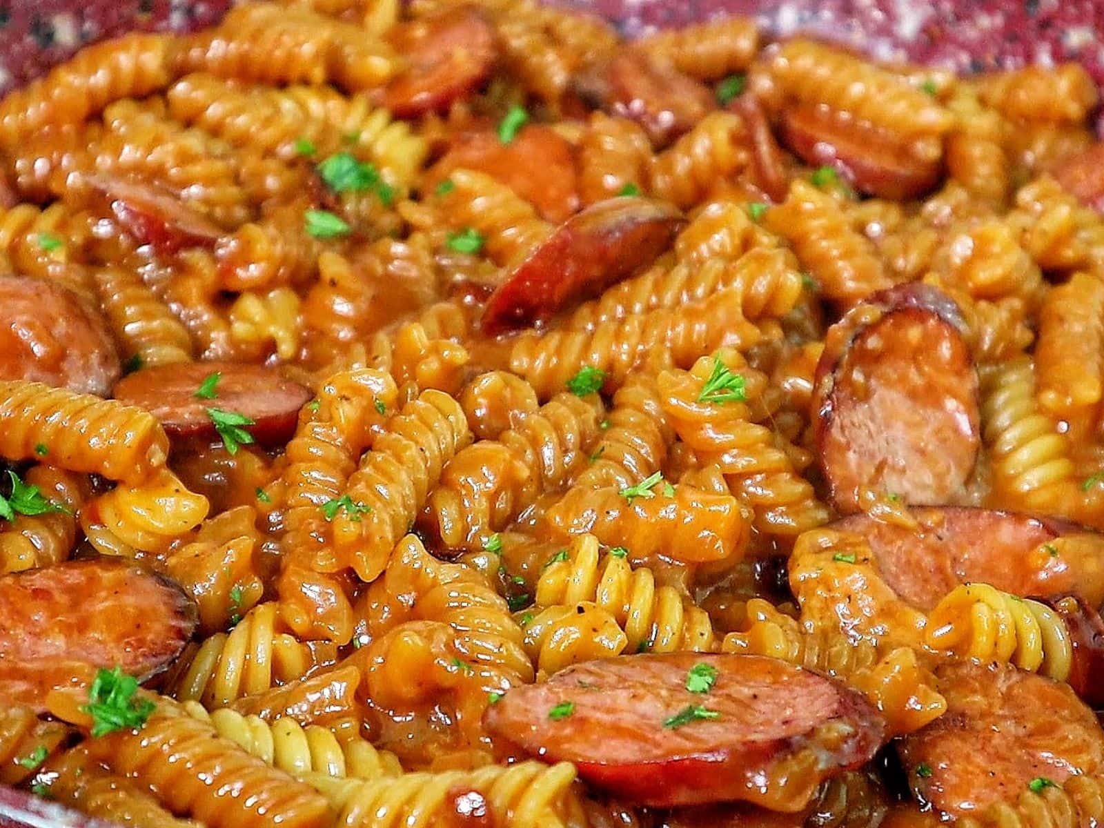 rotini pasta coated in a rich honey BBQ sauce with sliced sausage and garnished with fresh parsley