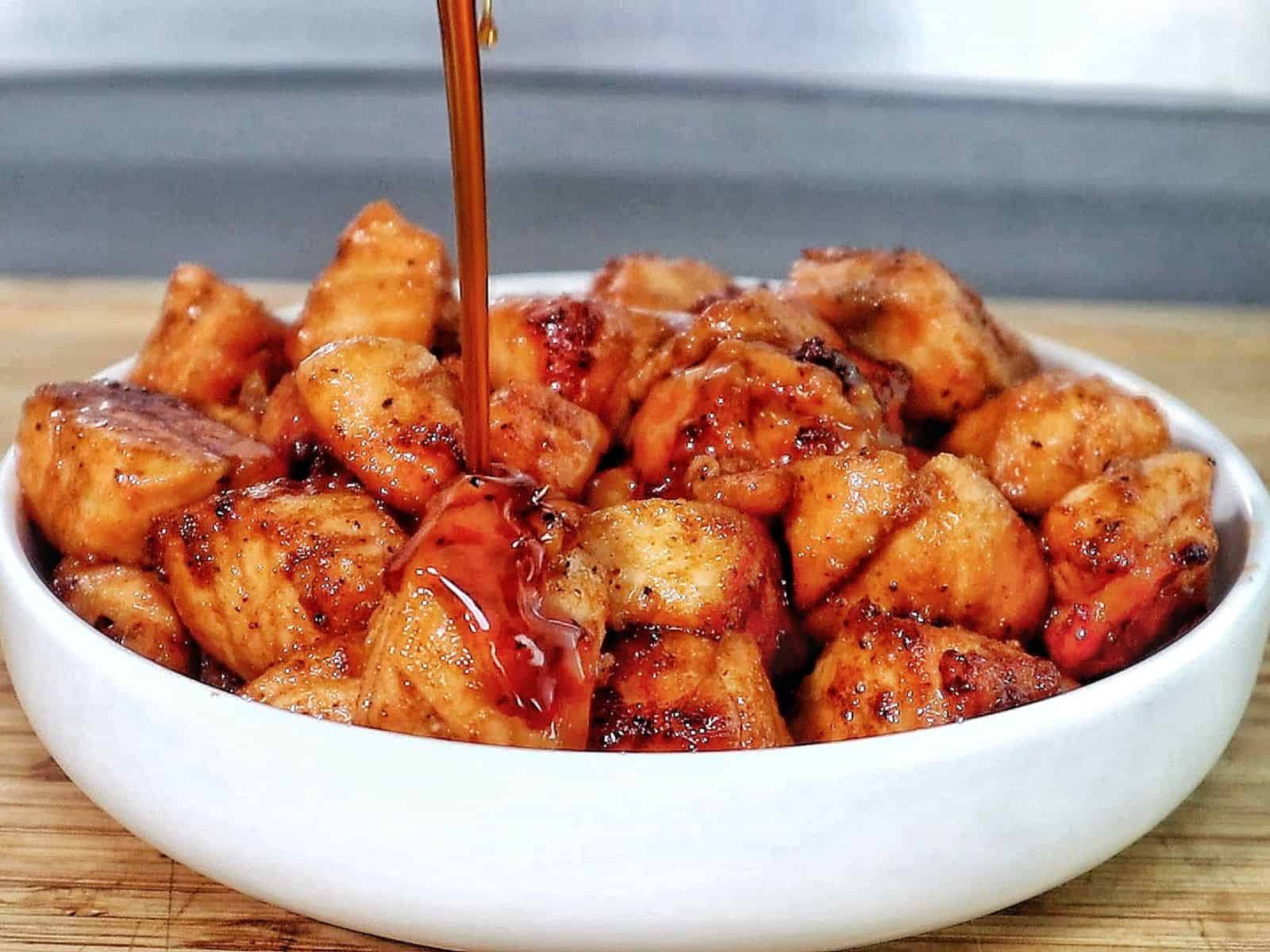 A white bowl filled with golden brown hot honey salmon bites, garnished with sesame seeds and fresh parsley.