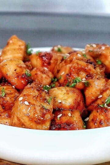 A white bowl filled with golden brown hot honey salmon bites, garnished with sesame seeds and fresh parsley.