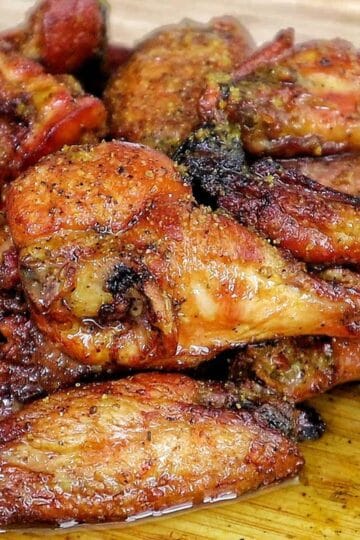 A close-up of golden-brown smoked chicken wings piled on a wooden cutting board, seasoned with a wet lemon pepper sauce from the grill.