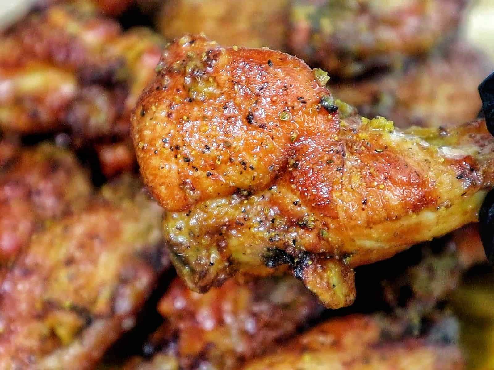 A close-up of golden-brown smoked chicken wings piled on a wooden cutting board, seasoned with a wet lemon pepper sauce from the grill.
