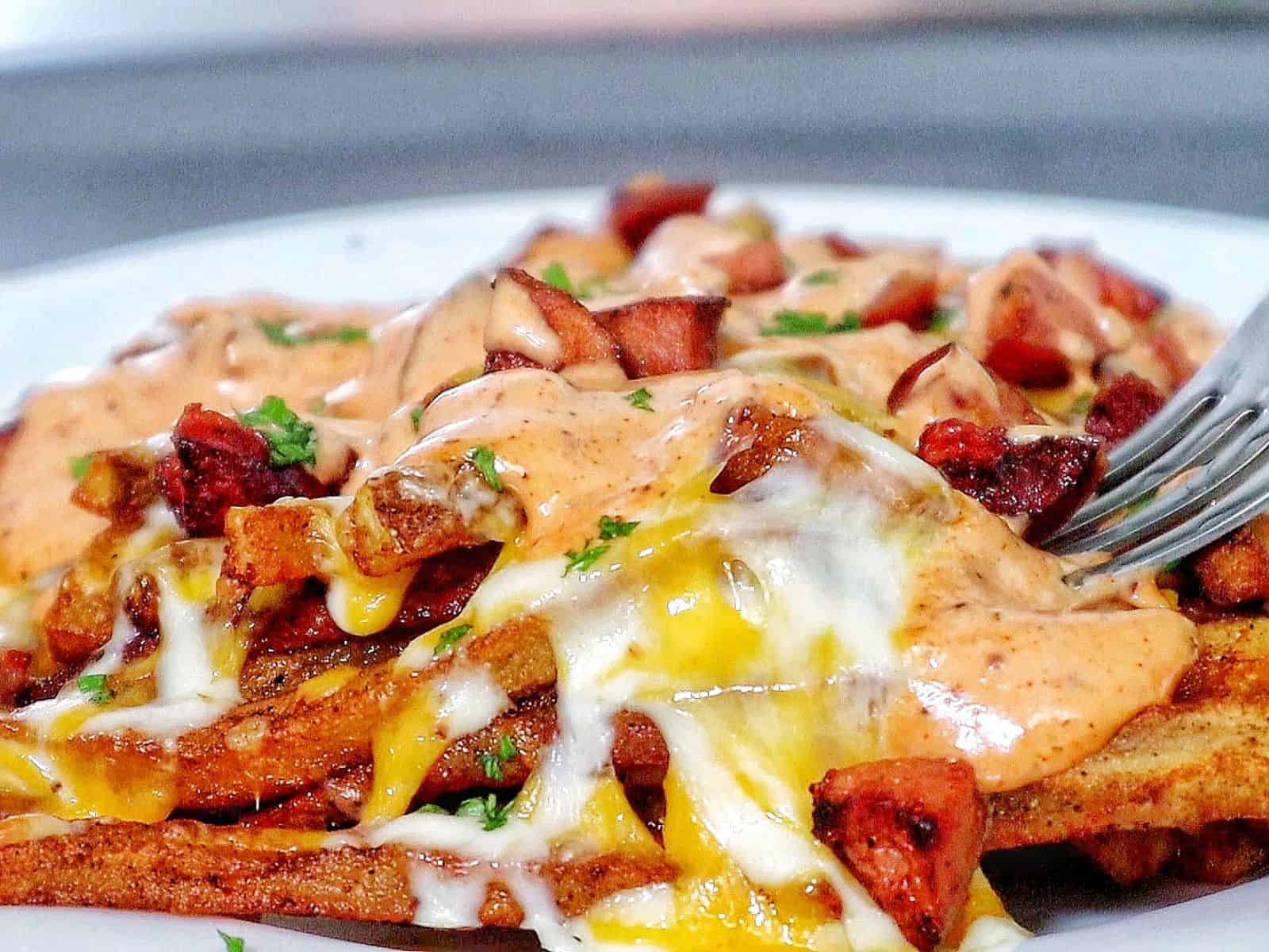 Golden, crispy French fries topped with melted cheese, Cajun sausage, and drizzled with spicy ranch-style sauce, garnished with fresh herbs.