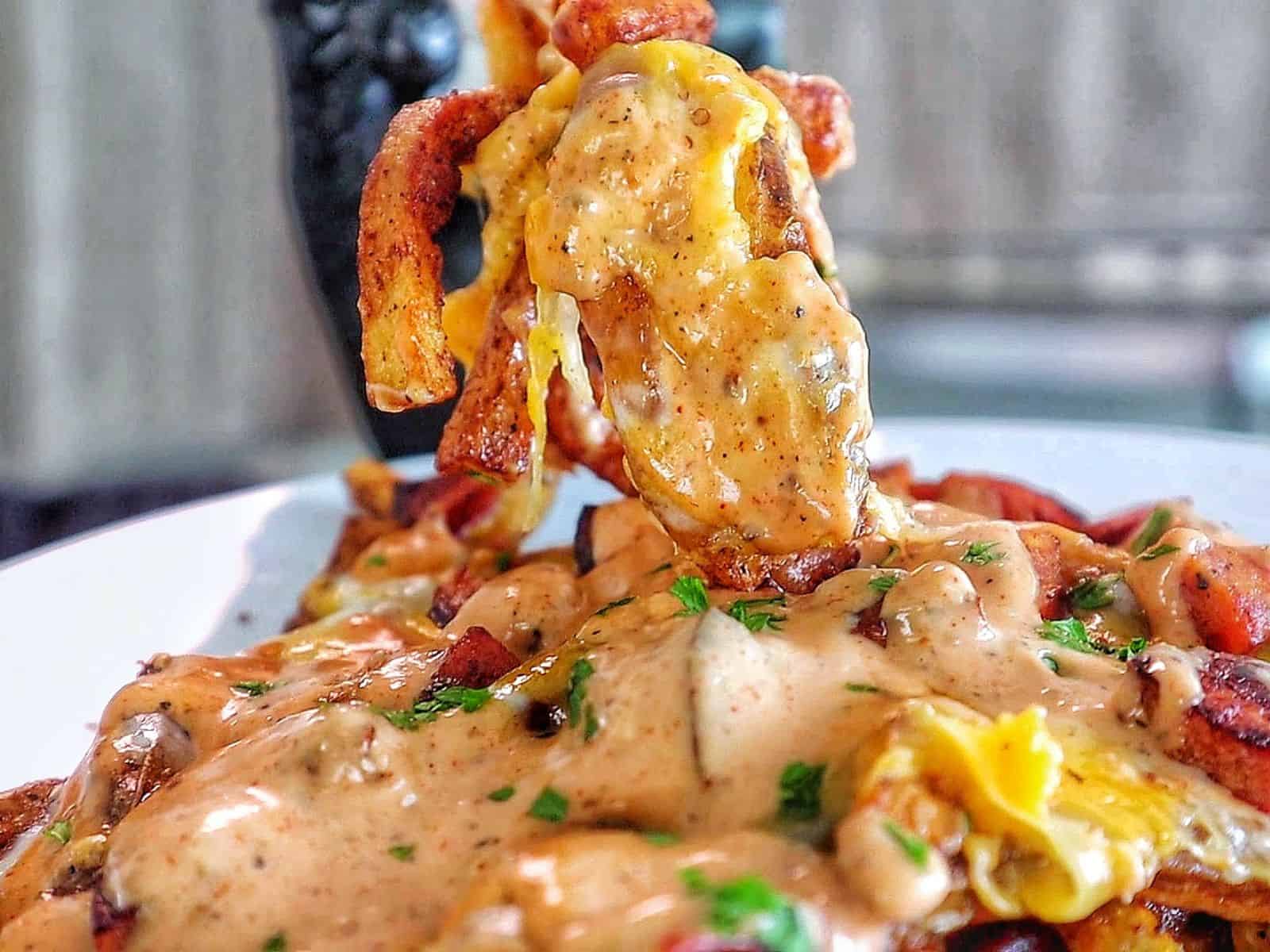 Golden, crispy French fries topped with melted cheese, Cajun sausage, and drizzled with spicy ranch-style sauce, garnished with fresh herbs.