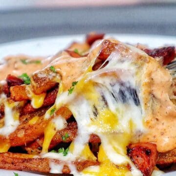 Golden, crispy French fries topped with melted cheese, Cajun sausage, and drizzled with spicy ranch-style sauce, garnished with fresh herbs.