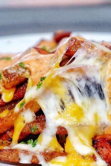 Golden, crispy French fries topped with melted cheese, Cajun sausage, and drizzled with spicy ranch-style sauce, garnished with fresh herbs.