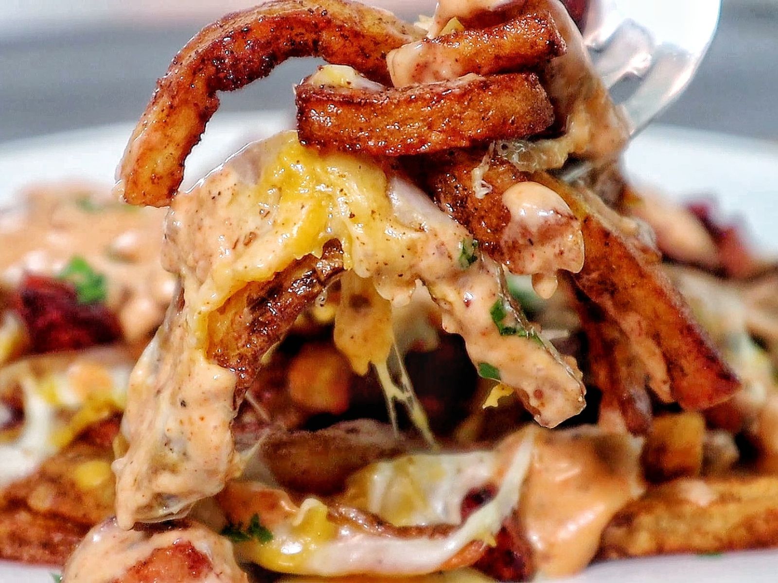 Golden, crispy French fries topped with melted cheese, Cajun sausage, and drizzled with spicy ranch-style sauce, garnished with fresh herbs.