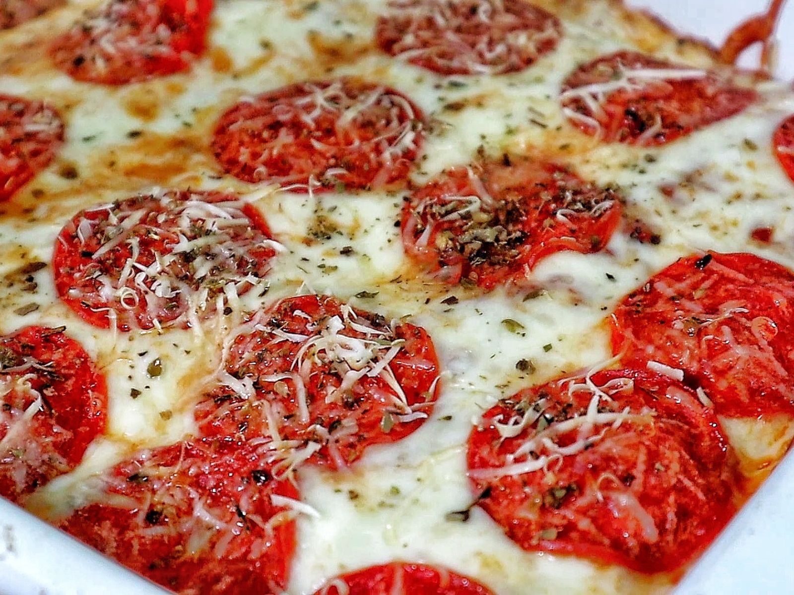 A baked Meat Lover's Pizza Enchilada casserole topped with melted mozzarella cheese, pepperoni slices, herbs, and grated Parmesan.