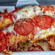 A baked Meat Lover's Pizza Enchilada casserole topped with melted mozzarella cheese, pepperoni slices, herbs, and grated Parmesan.