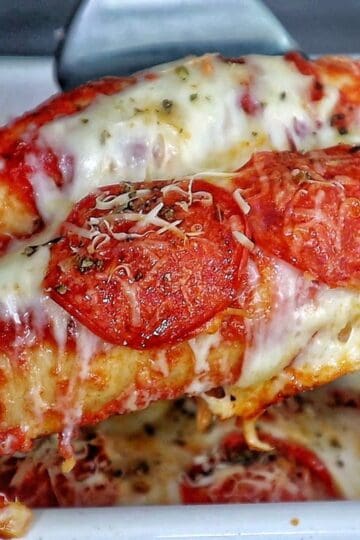 A baked Meat Lover's Pizza Enchilada casserole topped with melted mozzarella cheese, pepperoni slices, herbs, and grated Parmesan.