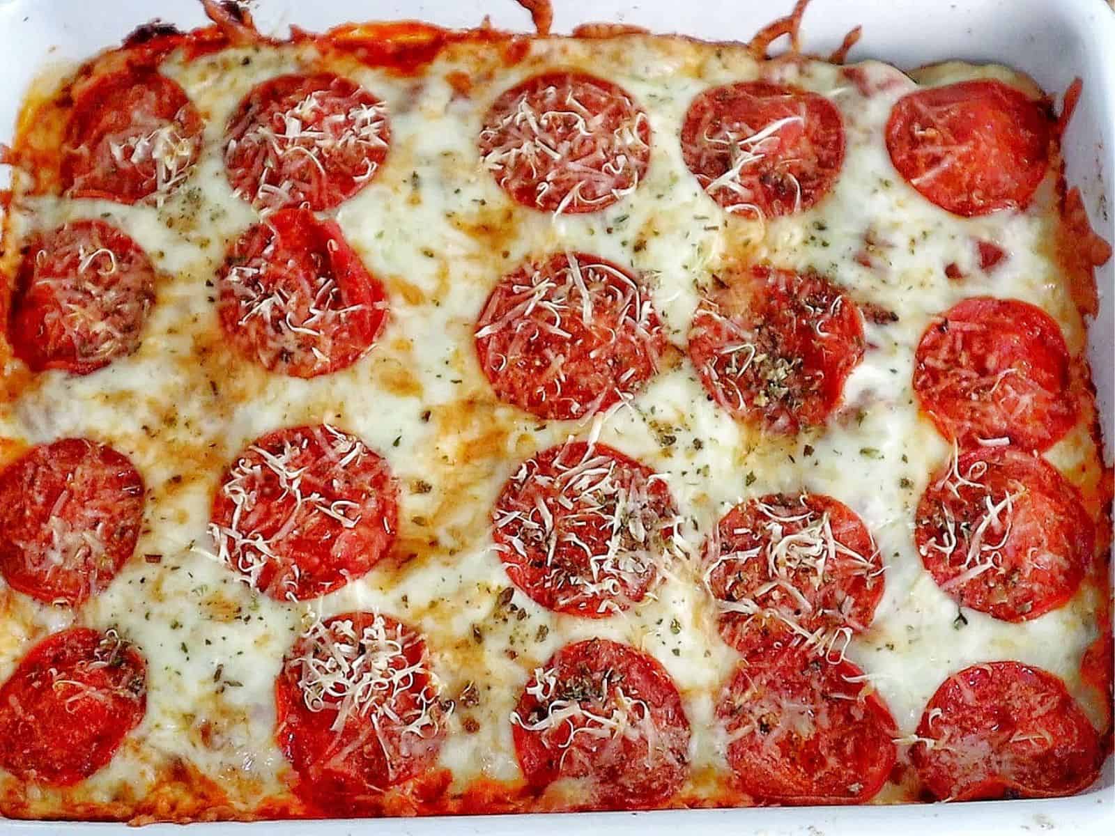 A baked Meat Lover's Pizza Enchilada casserole topped with melted mozzarella cheese, pepperoni slices, herbs, and grated Parmesan.