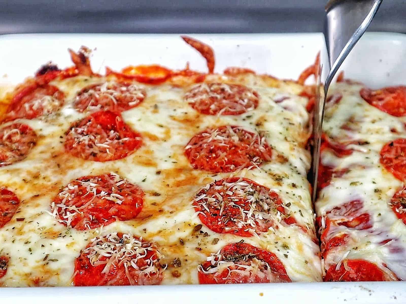 A baked Meat Lover's Pizza Enchilada casserole topped with melted mozzarella cheese, pepperoni slices, herbs, and grated Parmesan.