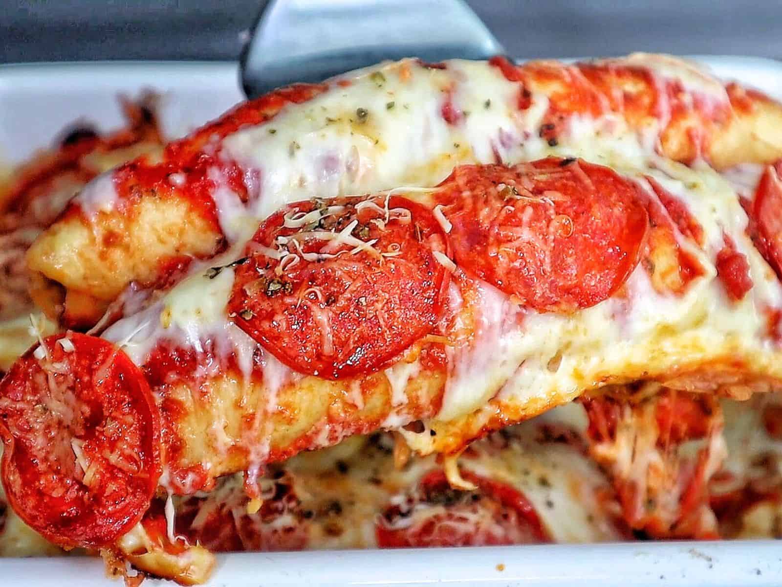 A baked Meat Lover's Pizza Enchilada casserole topped with melted mozzarella cheese, pepperoni slices, herbs, and grated Parmesan.