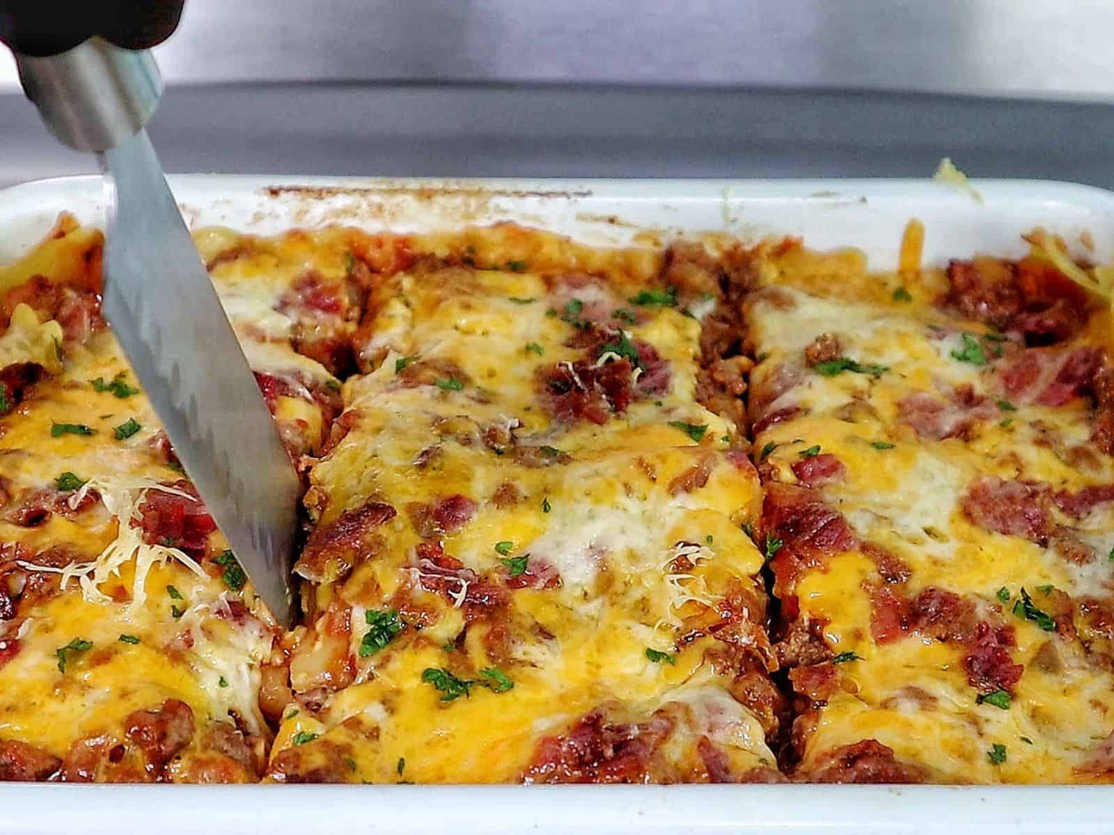 Parmesan garlic bacon cheeseburger lasagna layered with pasta, seasoned beef, crispy bacon, rich tomato sauce, and melted cheese, served on a white plate.