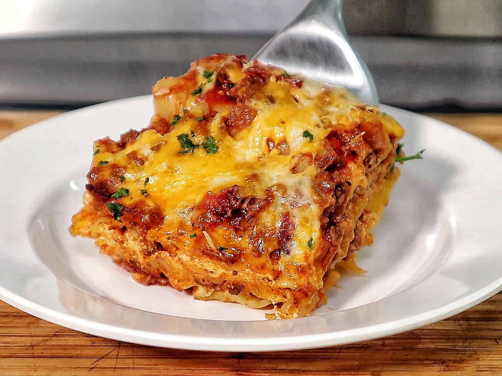 A slice of parmesan garlic bacon cheeseburger lasagna layered with pasta, seasoned beef, crispy bacon, rich tomato sauce, and melted cheese, served on a white plate.