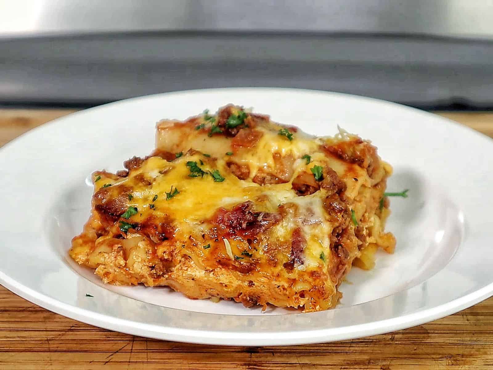 A slice of parmesan garlic bacon cheeseburger lasagna layered with pasta, seasoned beef, crispy bacon, rich tomato sauce, and melted cheese, served on a white plate.