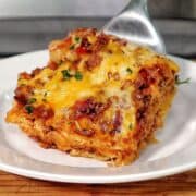 A slice of parmesan garlic bacon cheeseburger lasagna layered with pasta, seasoned beef, crispy bacon, rich tomato sauce, and melted cheese, served on a white plate.