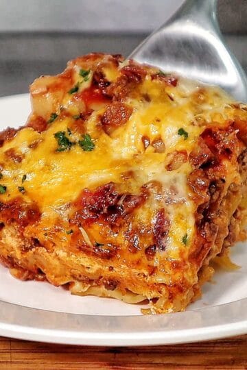 A slice of parmesan garlic bacon cheeseburger lasagna layered with pasta, seasoned beef, crispy bacon, rich tomato sauce, and melted cheese, served on a white plate.