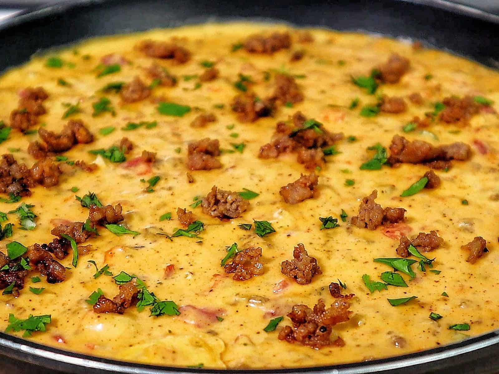 Creamy Ranch Rotel queso dip topped with browned sausage crumbles and garnished with fresh chopped parsley.