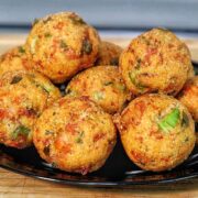 Golden brown shrimp stuffed hush puppies piled on a black plate inside a crispy fried cornmeal coating.