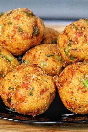 Golden brown shrimp stuffed hush puppies piled on a black plate inside a crispy fried cornmeal coating.