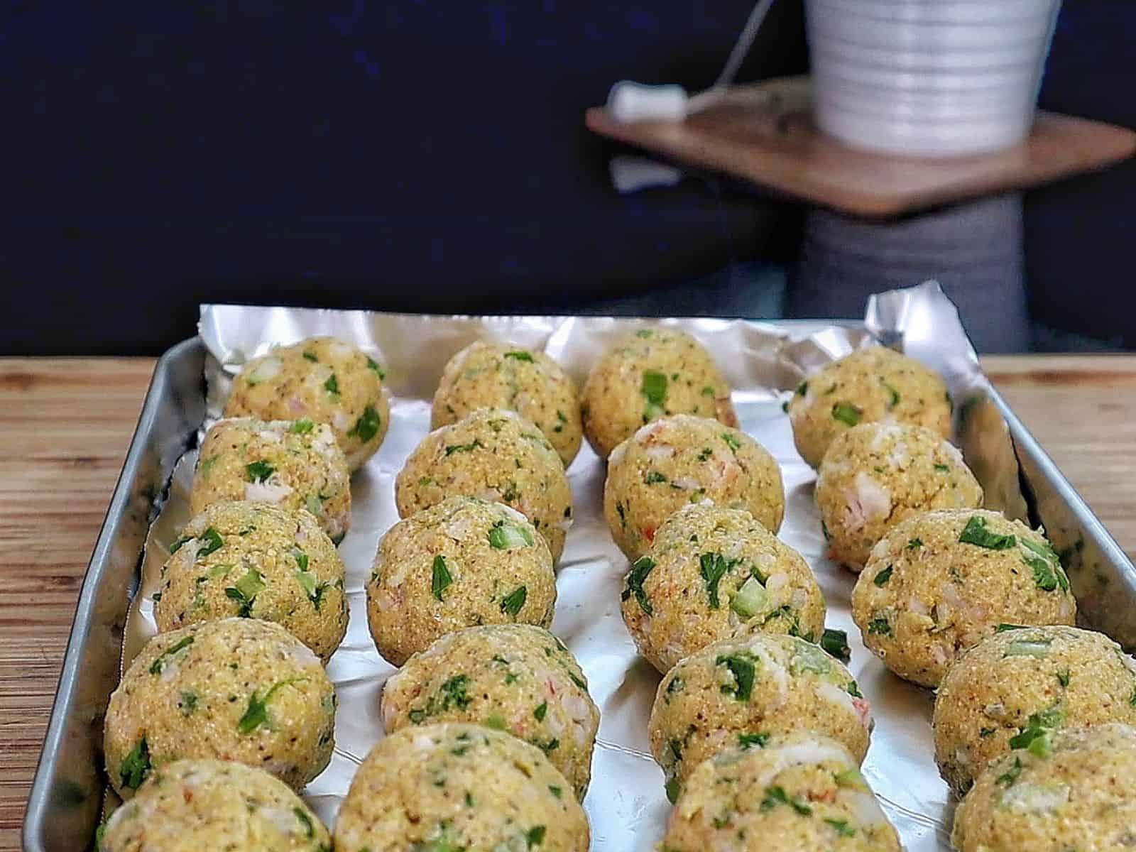 Golden brown shrimp stuffed hush puppies piled on a black plate inside a crispy fried cornmeal coating.