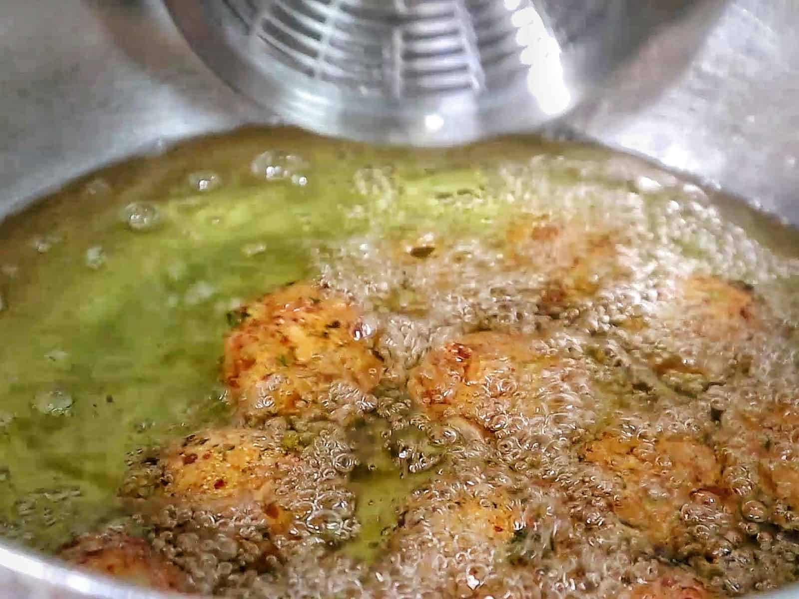 Golden brown shrimp stuffed hush puppies piled on a black plate inside a crispy fried cornmeal coating.