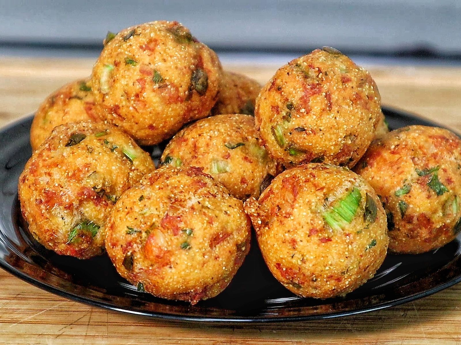 Golden brown shrimp stuffed hush puppies piled on a black plate inside a crispy fried cornmeal coating.