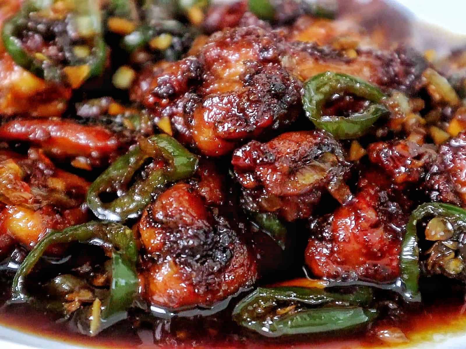 A plate of spicy jalapeño chicken thighs glazed in a honey, rich sauce, garnished with sliced jalapeños and minced garlic for a flavorful finish.